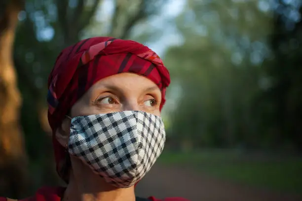 Photo of Mature woman wearing handmade textile face mask as accessory and protective element during sunny spring day in the park because of coronavirus pandemic
