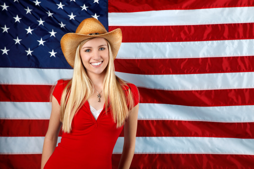 Carefree pretty girl running and smiling on the green field with a blowing flag of USA. Independence Day