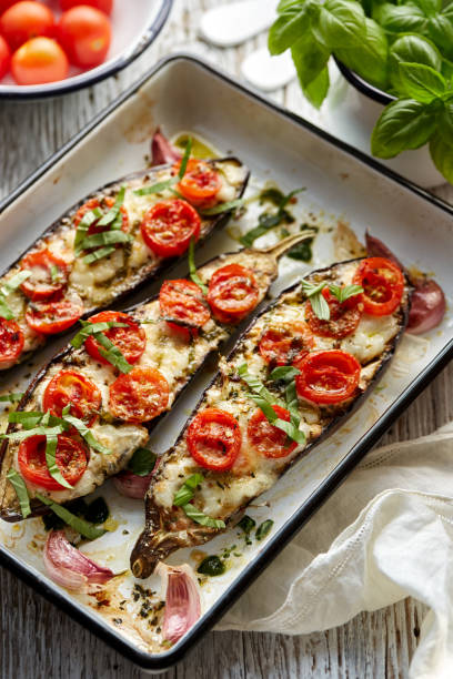 berenjenas rellenas al horno con queso, tomates cherry y albahaca en plato blanco de cazuela de esmalte - aubergines parmesan fotografías e imágenes de stock