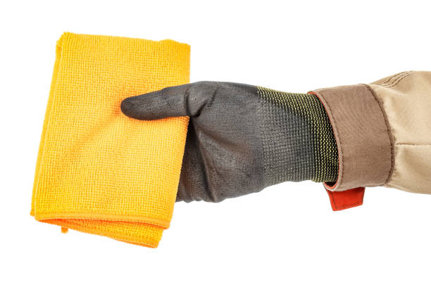 istock Clean orange microfiber cloth in worker hand in black protective glove and brown uniform isolated on white background 1235051236