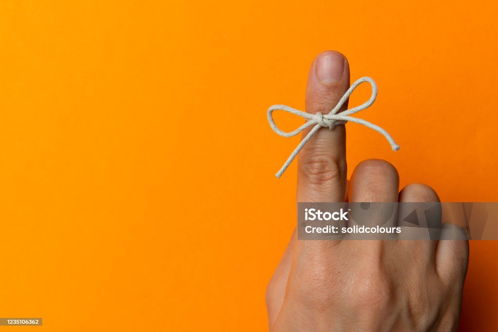 Hand and String Tied On Index Finger Hand and string tied on index finger on orange background. Reminder Stock Photo