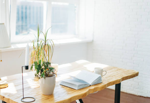 istock Wooden table with an open book by window in bright room Scandinavian interior 1235138562