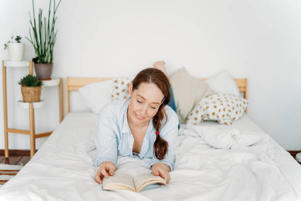 istock Friendly charming brunette woman reading book on bed in bright interior 1235139120