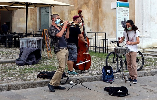 Udine, Italy. May 30, 2020. Street musicians play in the square with musical instruments and protective face masks, some days after the end of coronavirus lockdown