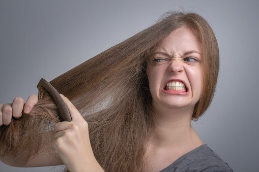 Young caucasian woman girl struggling to comb brush her straight hair with funny frustrated face. Long hair problem concept
