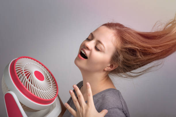 junge kaukasische frau mädchen mit langen haaren halten elektrischen ventilator vor ihrem gesicht. abkühlung bei heißem sommerwetterkonzept - electric fan women wind beautiful stock-fotos und bilder