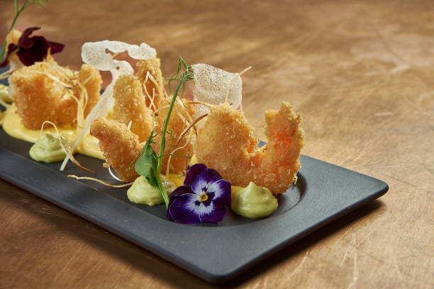 istock Appetizing deep-fried breaded tiger prawns with yellow sauce and rice chips on a black plate on a copper background. Close up. Seafood 1235179472