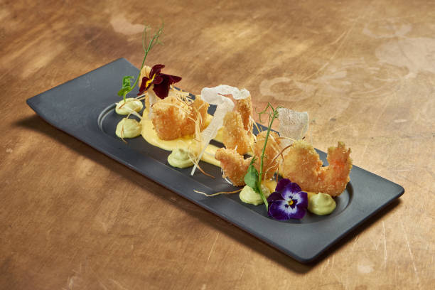 istock Appetizing deep-fried breaded tiger prawns with yellow sauce and rice chips on a black plate on a copper background. Close up. Seafood 1235179975
