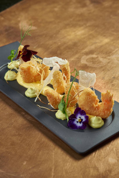 istock Appetizing deep-fried breaded tiger prawns with yellow sauce and rice chips on a black plate on a copper background. Close up. Seafood 1235180503