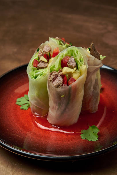 istock Appetizing spring rolls with beef, mango, cucumber and bell pepper with hot sauce in a red ceramic plate on a copper background 1235182087