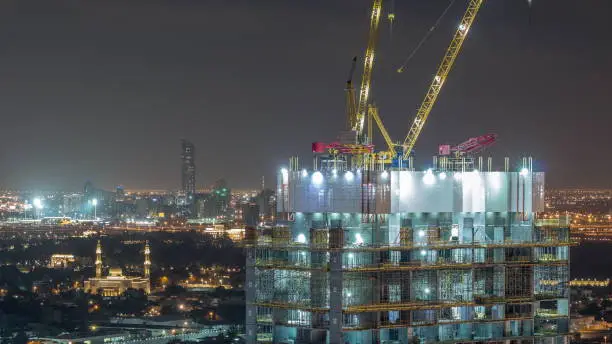 Construction activity in Dubai downtown with cranes and workers night timelapse, UAE. Building of new skyscrapers and towers
