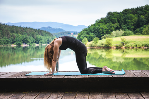 Woman doing yoga on the wooden floor by the lake. Cat pose (Marjaryasana).