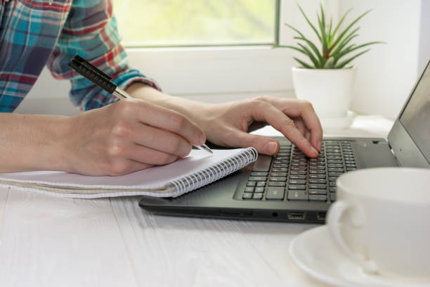 istock Hands with pen writing in notebook. Modern workplace for distance learning at home with black laptop 1235300644