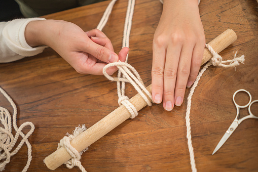 female hands doing macrame handcraft hobby - hands of woman at home table doing macramé netting using ropes, cords and threads in domestic handmade decoration