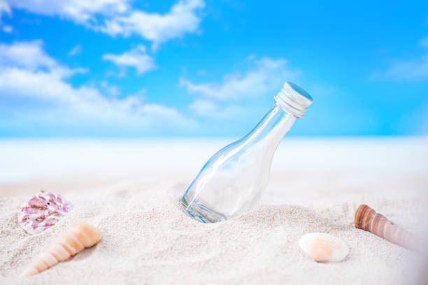 istock bottle on sand beach with seashell over blurred tropical blue sea and clear blue sky 1235337023