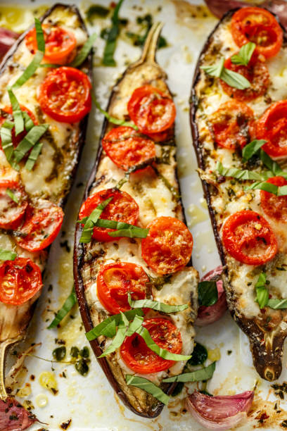 istock Grilled eggplants, stuffed with cheese and cherry tomatoes sprinkled chopped basil  on white background 1235357403