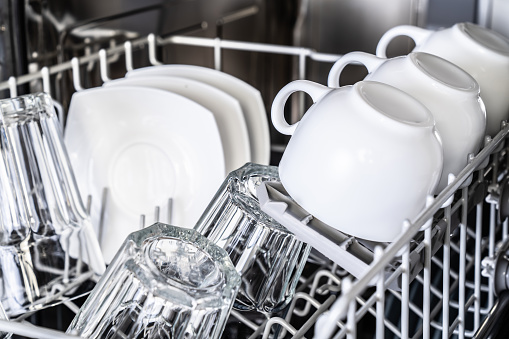White cups in new dishwasher close-up. Clean dishes. Housekeeping devices.