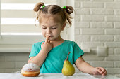 little girl chooses between donut and fruit. the concept of proper nutrition, the right choice