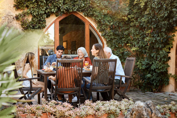 Multi-generation family having food in backyard Family talking while enjoying food together. Males and females are sitting at dining table against creeper plant. They are spending leisure time in backyard during weekend. spanish breakfast stock pictures, royalty-free photos & images