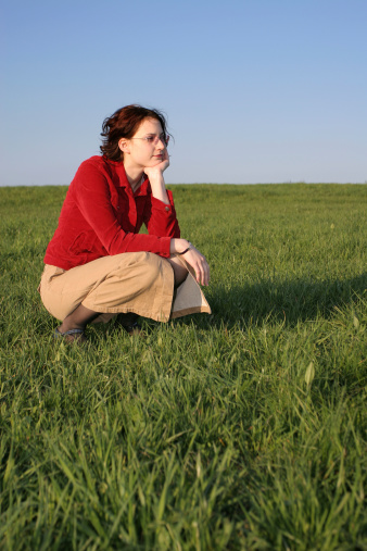 Girl on a big lawn. Kneeling and thinking.
