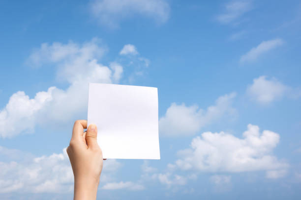 istock Woman hand holding white paper with sky and cloud background. 1235454570