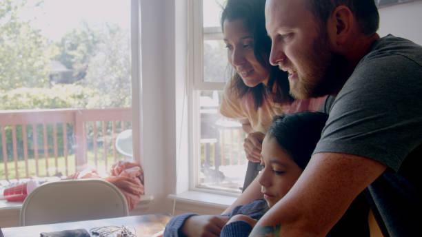 istock Young Mixed-Race Family huddled together in front of a laptop computer doing a video chat with a distant loved one 1235455111