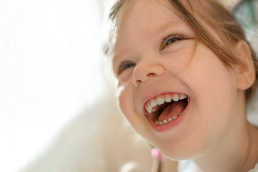 Little girl in cheerful mood with bright face and white teeth smiles and laughs. A portrait of child with bright eyes in soft focus. Her happy face is a reaction to the gift.