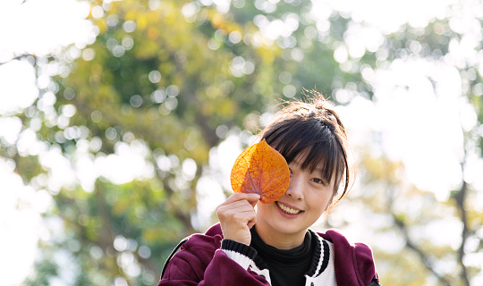 Woman covering eye with hibiscus leaf in autumn.