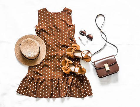Summer brown polka dot sleeveless dress, suede sandals, leather crossbody bag, sunglasses and hat on a light background, top view