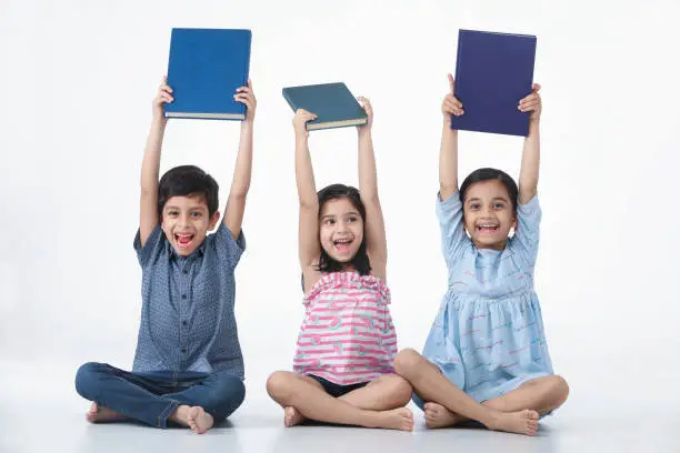 Group of Indian, Asian Kids Boys and Girl Sitting and Cheering with Books Above Their Head
