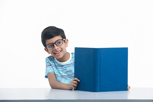 Indian, Asian Kid Child Boy with eye glasses Reading and Peeking Out Of The Living Book and Giving Happy Expressions