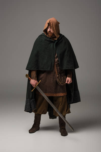 medieval Scottish redhead knight in mantel with sword on grey background