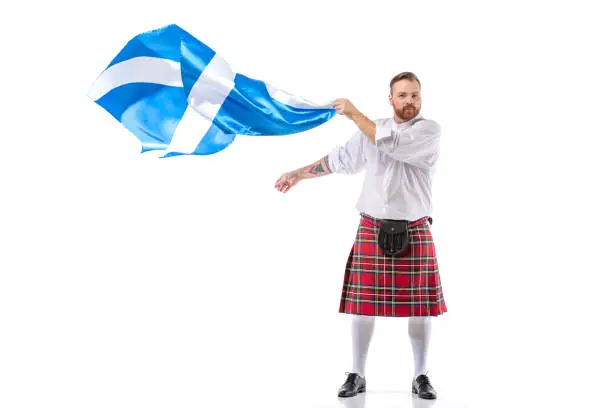 Scottish redhead man in red kilt with flag of Scotland on white background