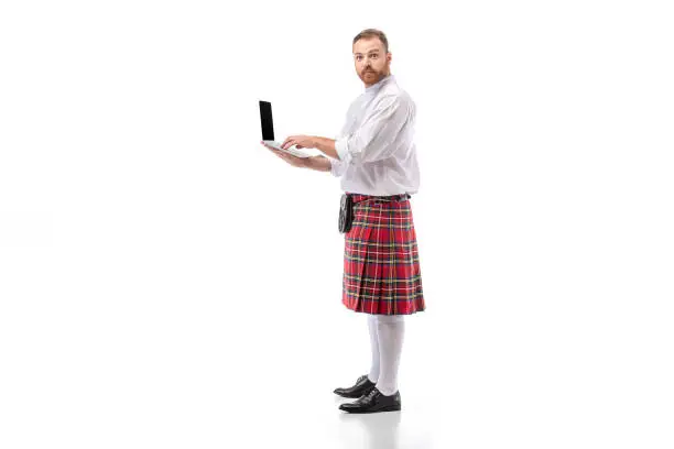 Scottish redhead man in red kilt holding laptop on white background