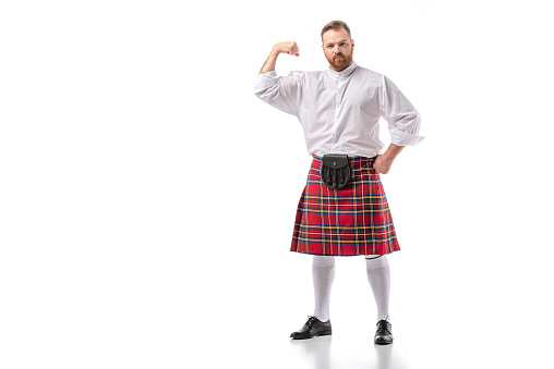strong Scottish redhead bearded man in red tartan kilt showing biceps on white background