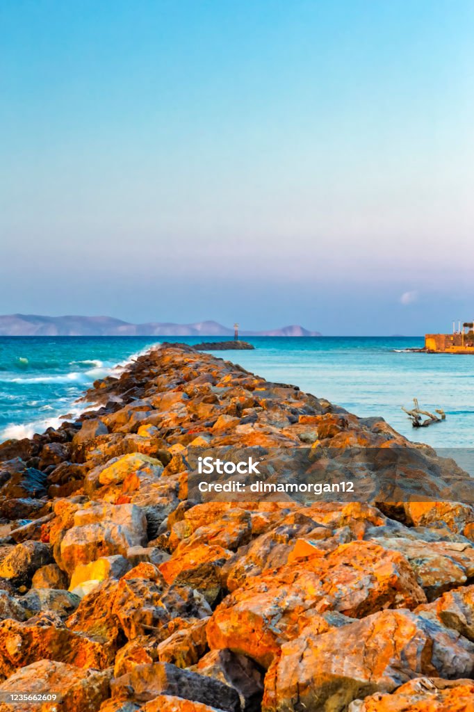 Long Stony Spit Going Far to Sea in Heraklion City on Crete, Greece. Roaring Waves Batter Against The Rocks During Golden Hour. Vertical Image Beach Stock Photo