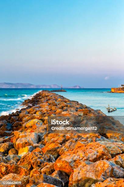 Long Stony Spit Going Far To Sea In Heraklion City On Crete Greece Roaring Waves Batter Against The Rocks During Golden Hour Vertical Image Stock Photo - Download Image Now