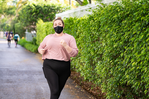 This is a photograph of a body positive Caucasian woman in her 30s exercising outdoors on the Aventura Circle fitness trail in Miami, Florida.