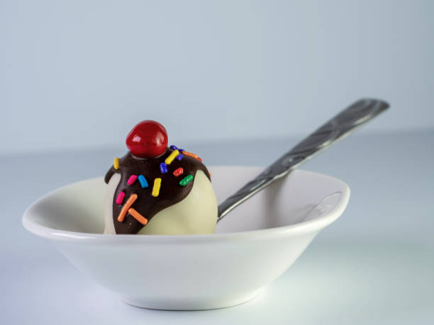 istock Banana Split Cake Ball Sitting in a Small White Bowl with a Spoon on a White Background.  Delicious Dessert like a Truffle. 1235753158