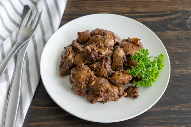 A plate of chicken livers fried with tomato and spices and garnished with a sprig of parsley
