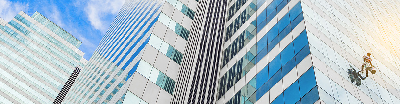 The worker cleaning glass window at the high rise building with the hanging rope climber. Glass windows building cleaning service. Risky service. Special Job concept.