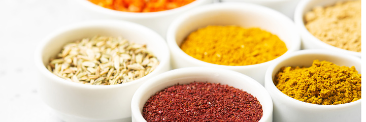 Spices in white bowls on a light gray table. Turmeric, ginger, curry, fennel and sumac in white bowls. Spices closeup with space for text. Banner