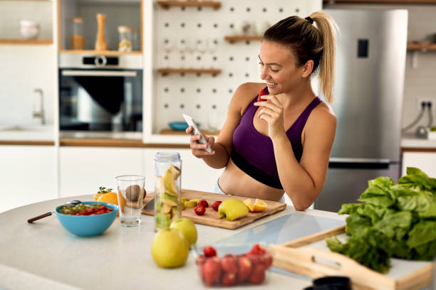 istock Happy sportswoman texting on cell phone while eating fruit in the kitchen. 1235850154