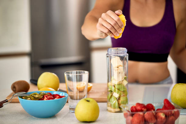 istock Close-up of sportswoman using lemon while making fruit smoothie at home. 1235853290