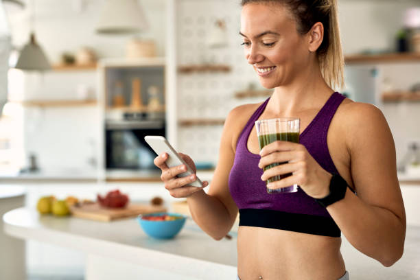 istock Happy athletic woman drinking smoothie and using mobile phone in the kitchen. 1235854671