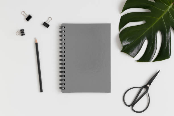 istock Top view of a grey notebook mockup with  workspace accessories and a monstera leaf on a white table. 1235879010