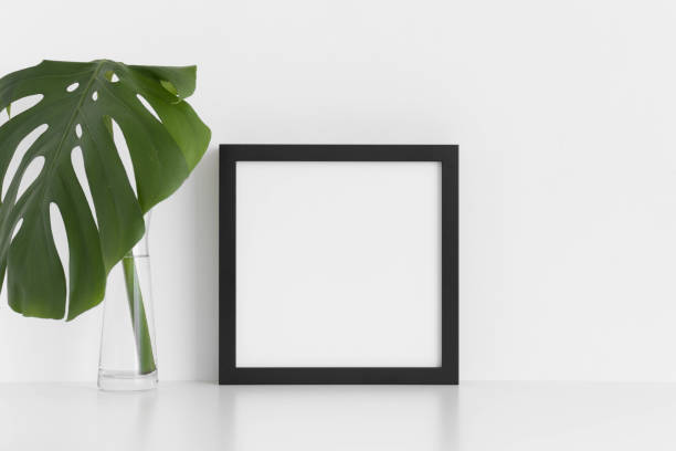 istock Black square frame mockup with a monstera leaf in a glass vase on a white table. 1235904928