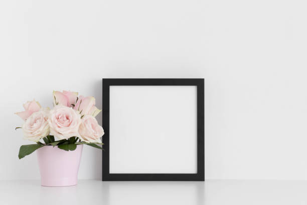 istock Black square frame mockup with pink roses in a pot on a white table. 1235905956