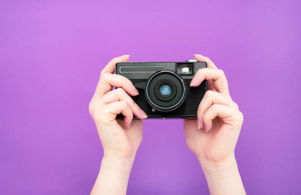istock black manual retro camera in hand on a purple background. isolate. banner 1235933570