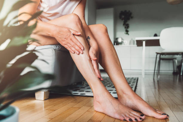 unrecognizable woman massaging body lotion on her legs - massage creme imagens e fotografias de stock